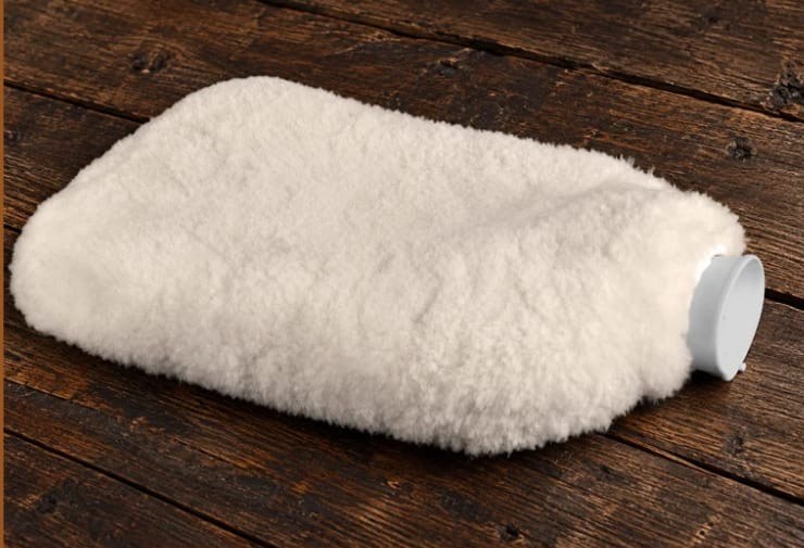 Warmwaterkruik met witte vachthoes op een houten vloer
