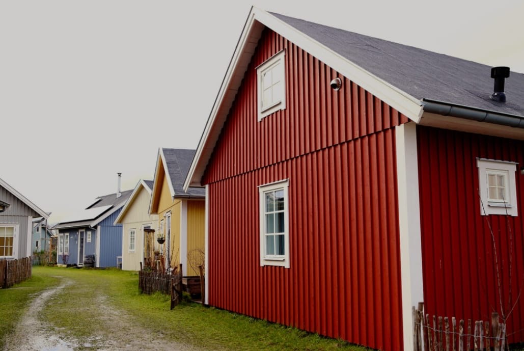 Rij houten huisjes in rood, geel, blauw en grijs langs een grasveld